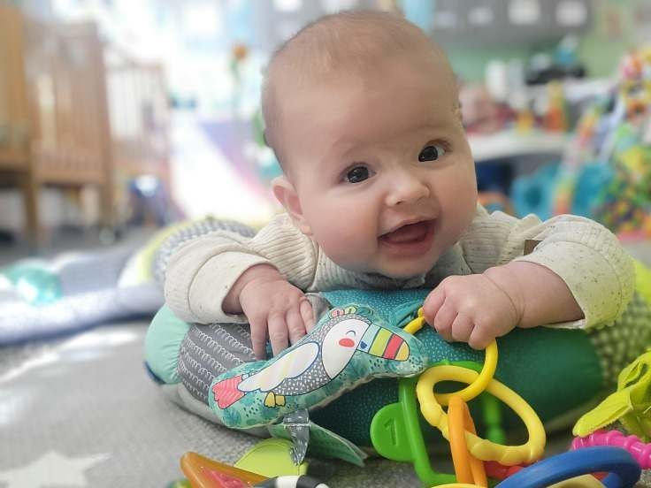 A baby is laying on a pillow playing with toys.