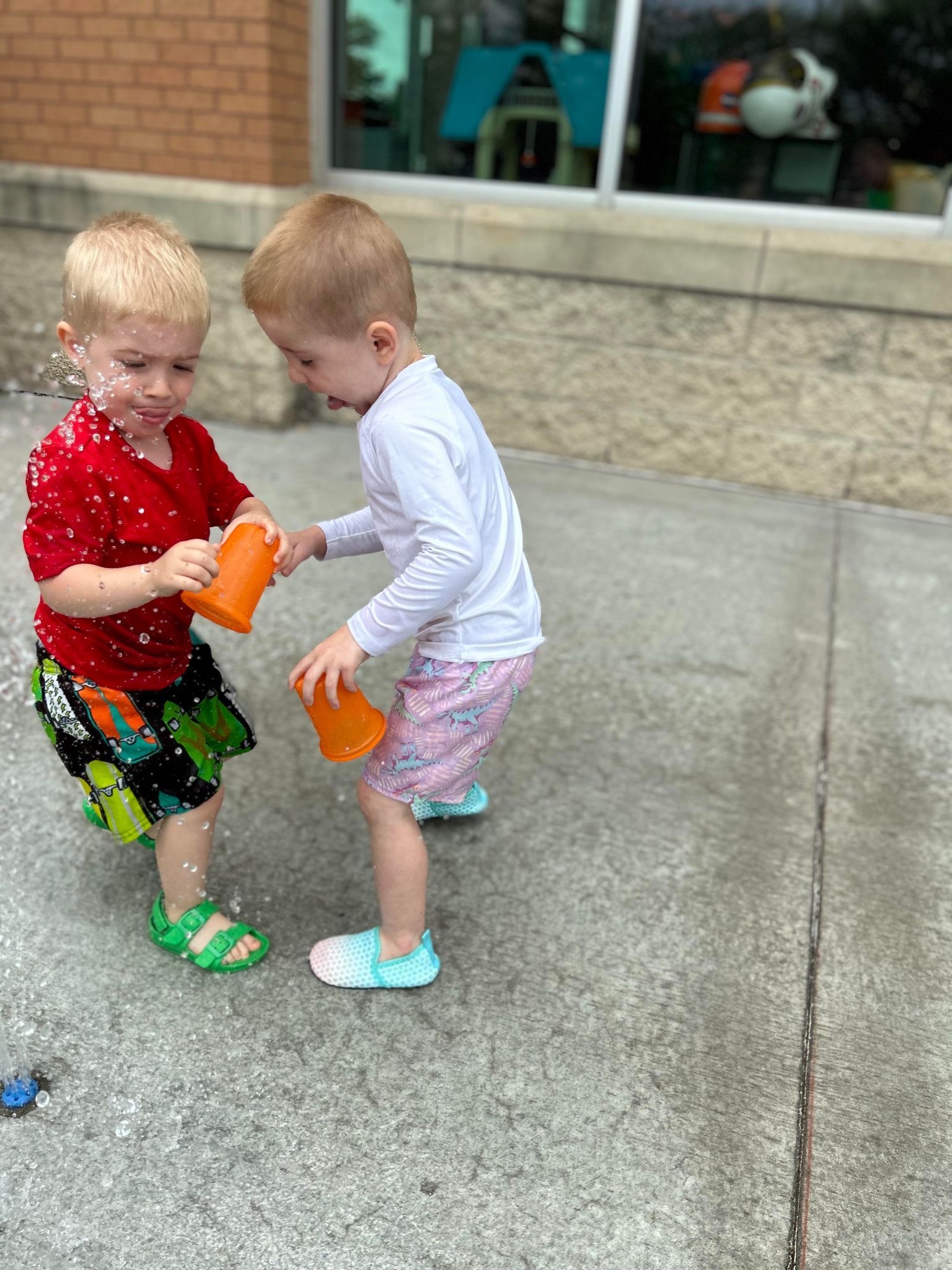 Two young boys are playing with water on the sidewalk.