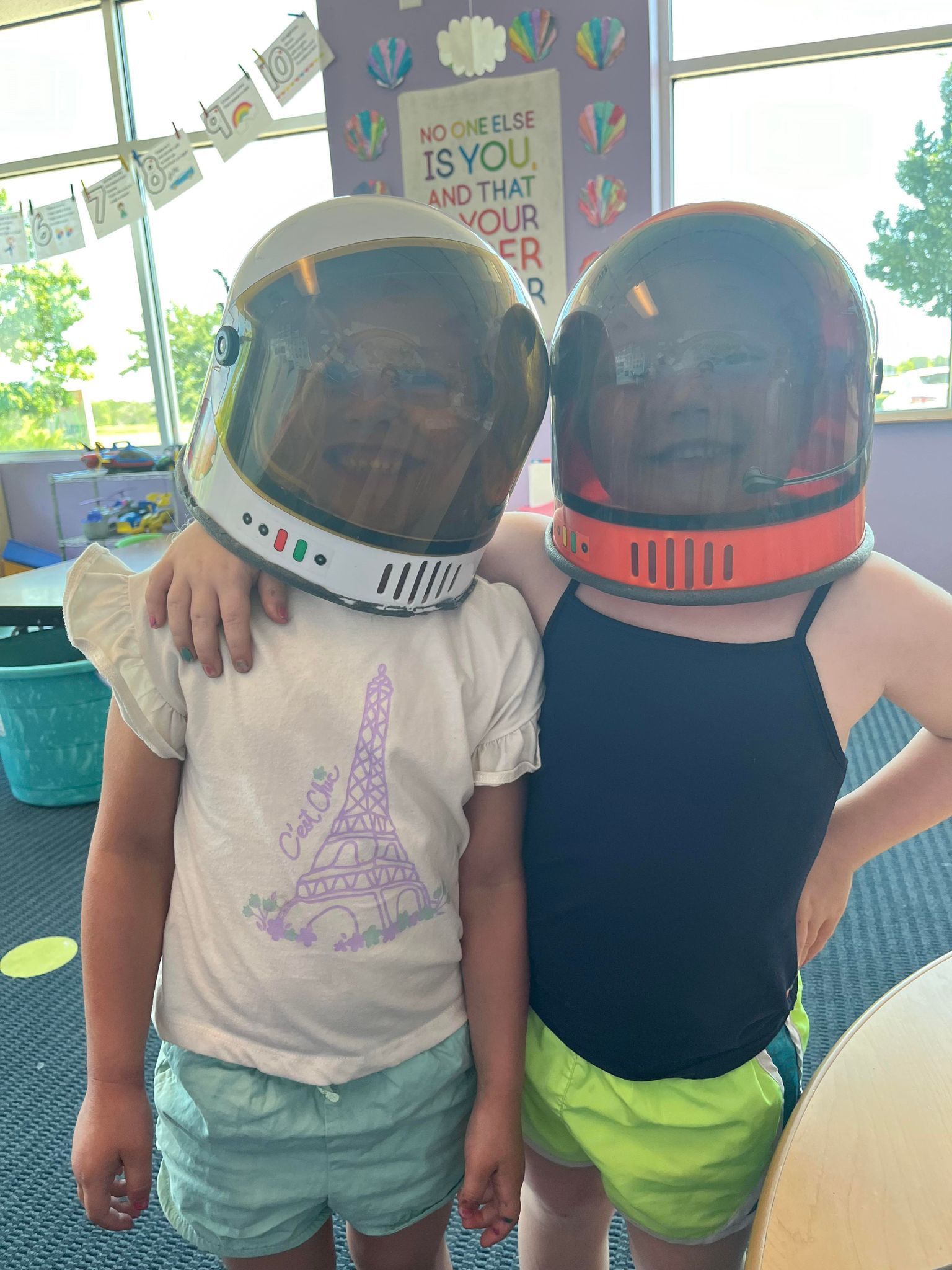 Two young girls wearing space helmets are standing next to each other.