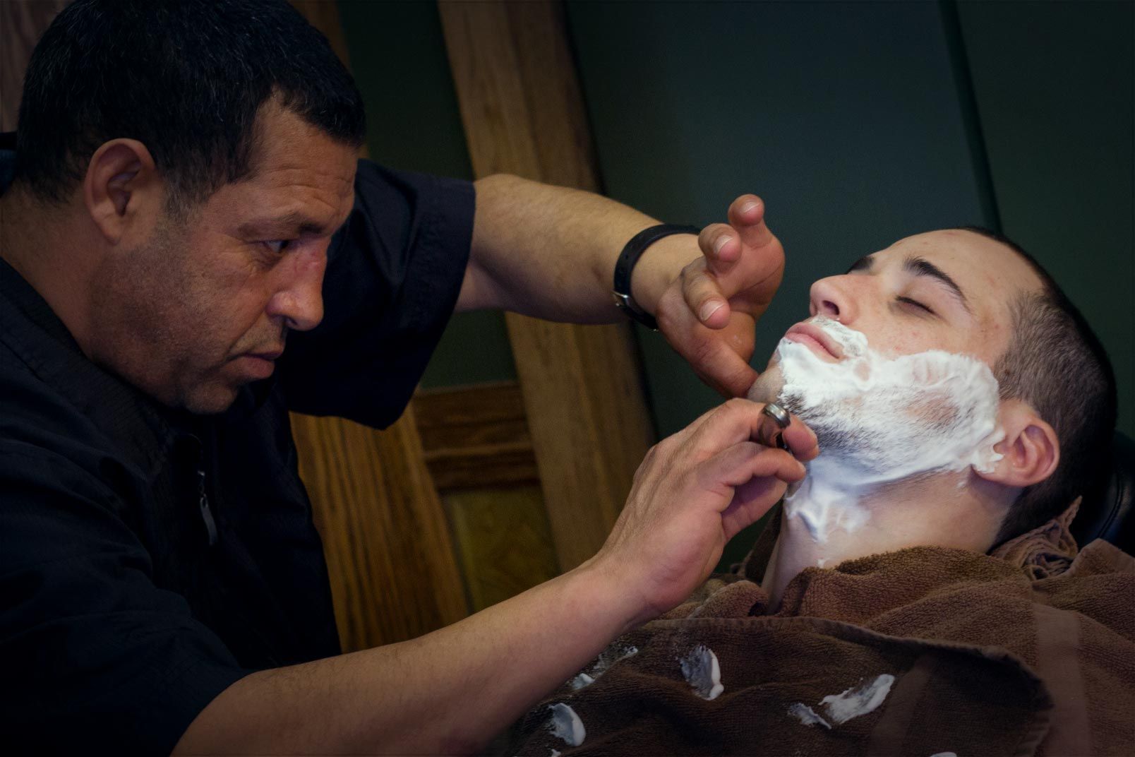 A man is shaving another man 's face with a razor.