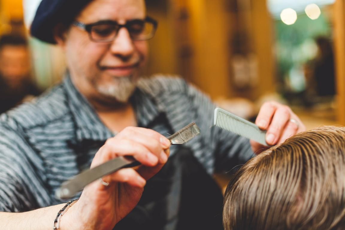 A man is cutting a man 's hair with a razor and comb.