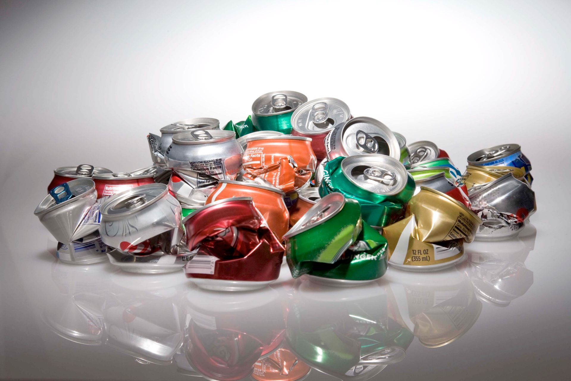 Crushed aluminum cans in various colors, piled on a reflective surface.