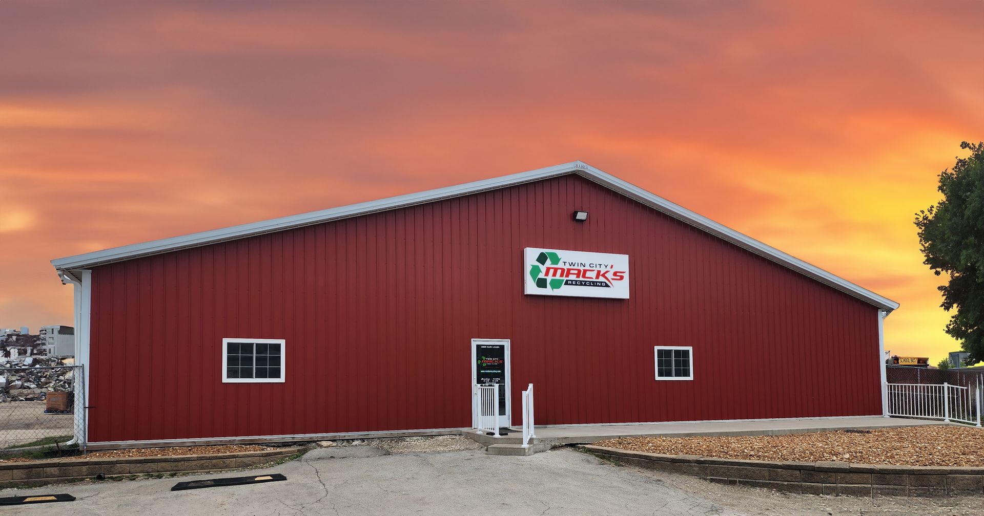 Red commercial building with white trim, sign above entrance, and sunset background.