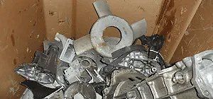 Pile of scrap metal parts, likely aluminum, in a wooden container.