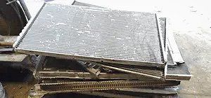 Pile of used vehicle radiators. Gray, metal fins stacked atop each other, viewed from above.