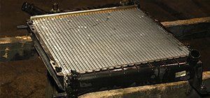 A car radiator with its cooling fins. Dark, gritty setting, possibly a repair shop.