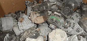 Pile of old, gray car alternators in a wooden bin.