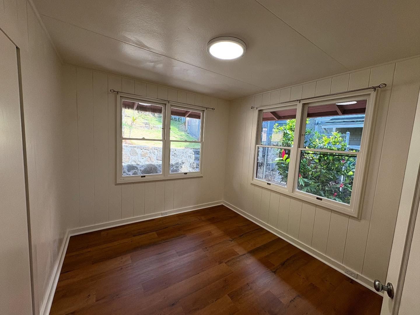 Empty room with hardwood floors, two windows, and a ceiling light. White walls and window frames.