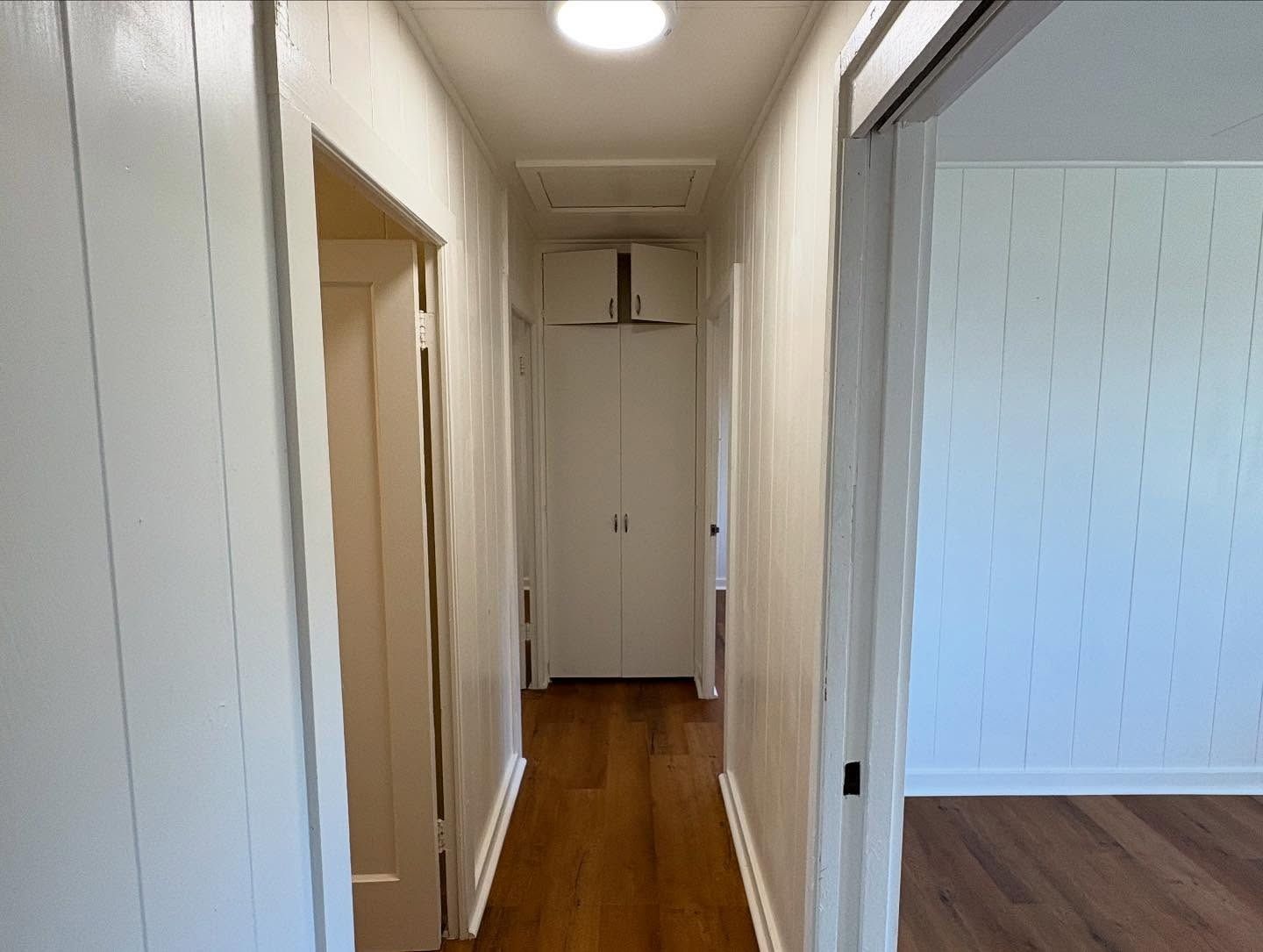 Narrow hallway with white walls and wood floor, leading to a closed white door.