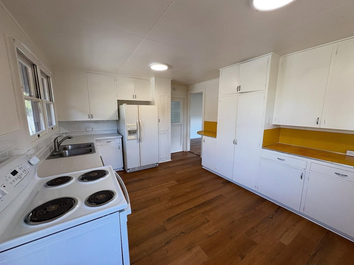 White kitchen with wooden floors, white appliances, and cabinets. A yellow countertop accents the wall cabinets.