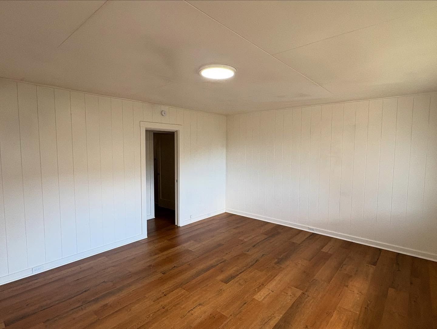 Empty room with wood floors, white paneled walls, and a round ceiling light.