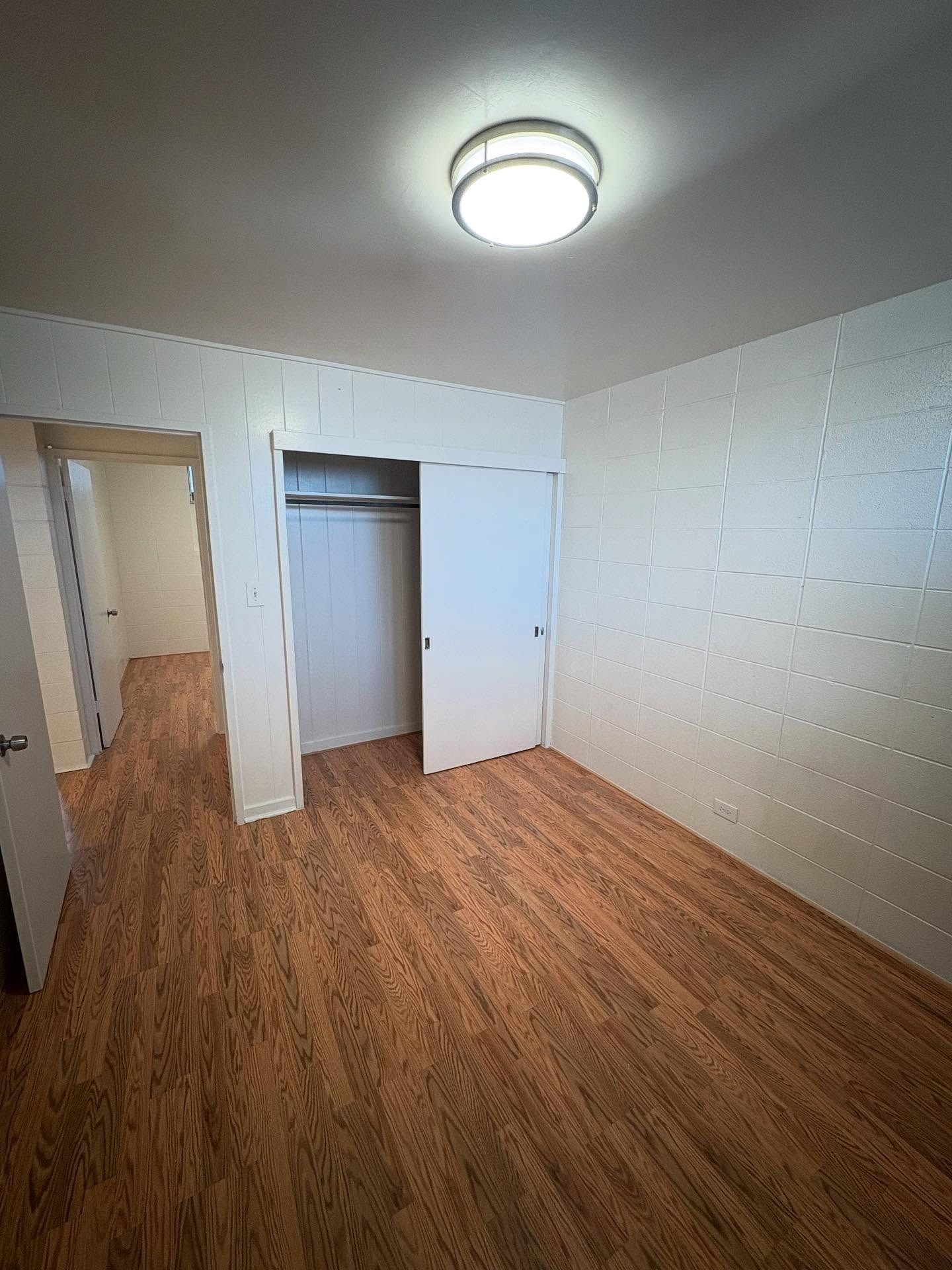 Empty bedroom with wooden floor, white walls, closet, and ceiling light.