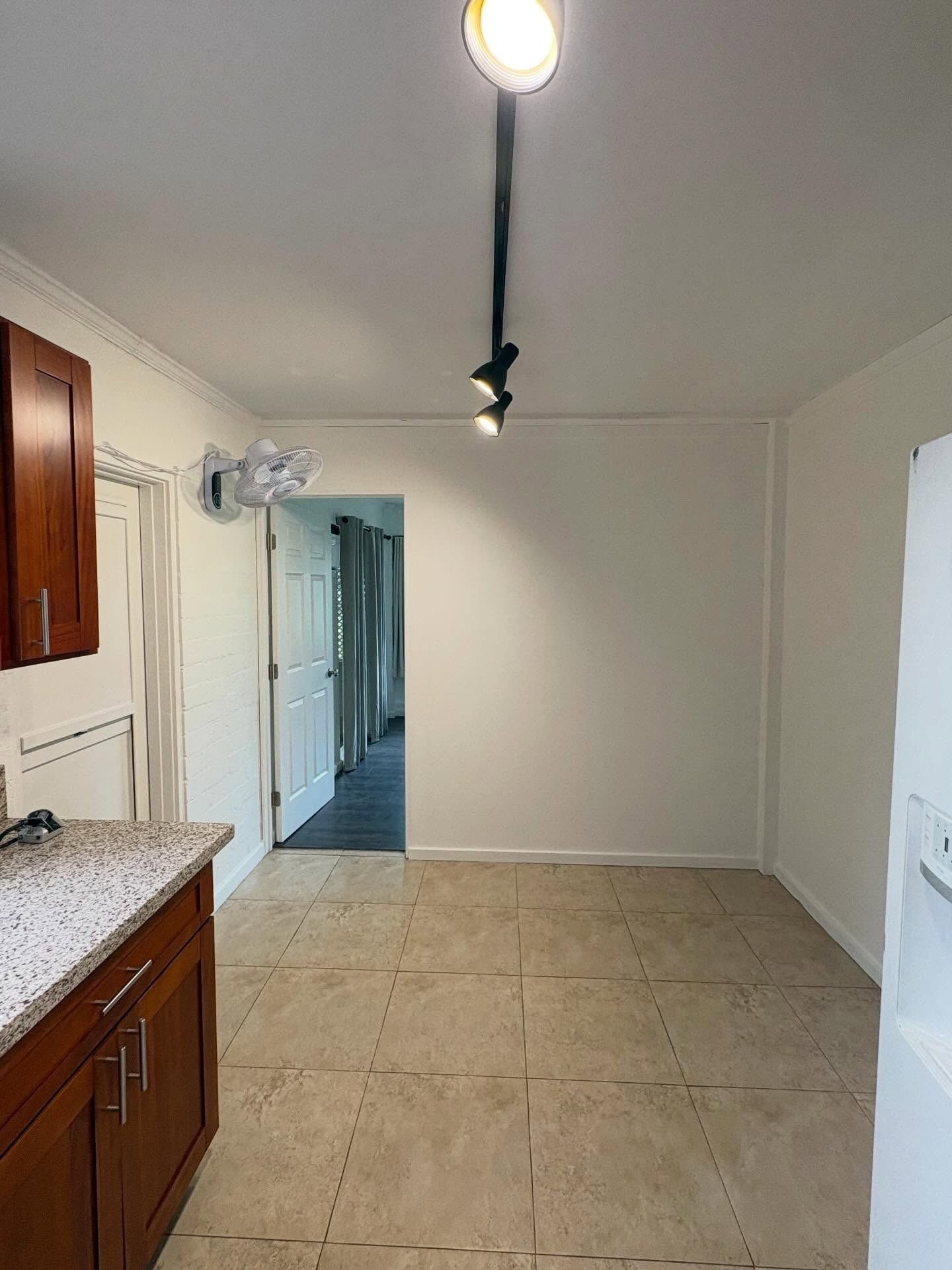 Kitchen with wooden cabinets, tile floor, white walls, and a hallway doorway.