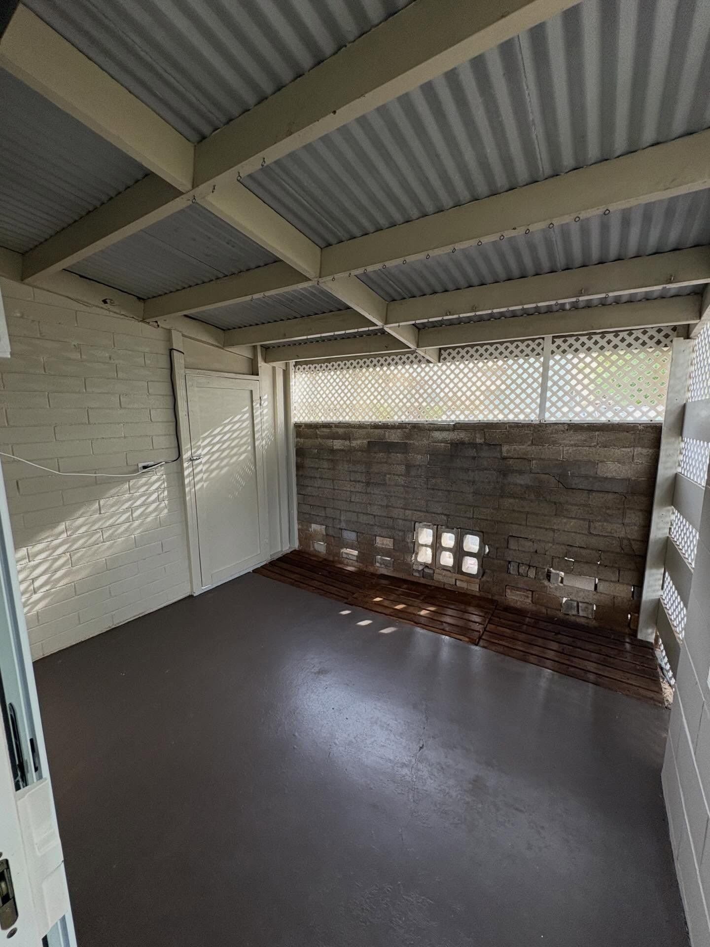 Covered patio with corrugated metal roof, brick wall, and painted white wooden beams.
