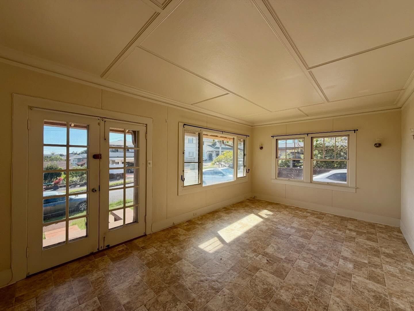 Empty sunlit room with french doors and windows; tan walls, tile floor, white ceiling.