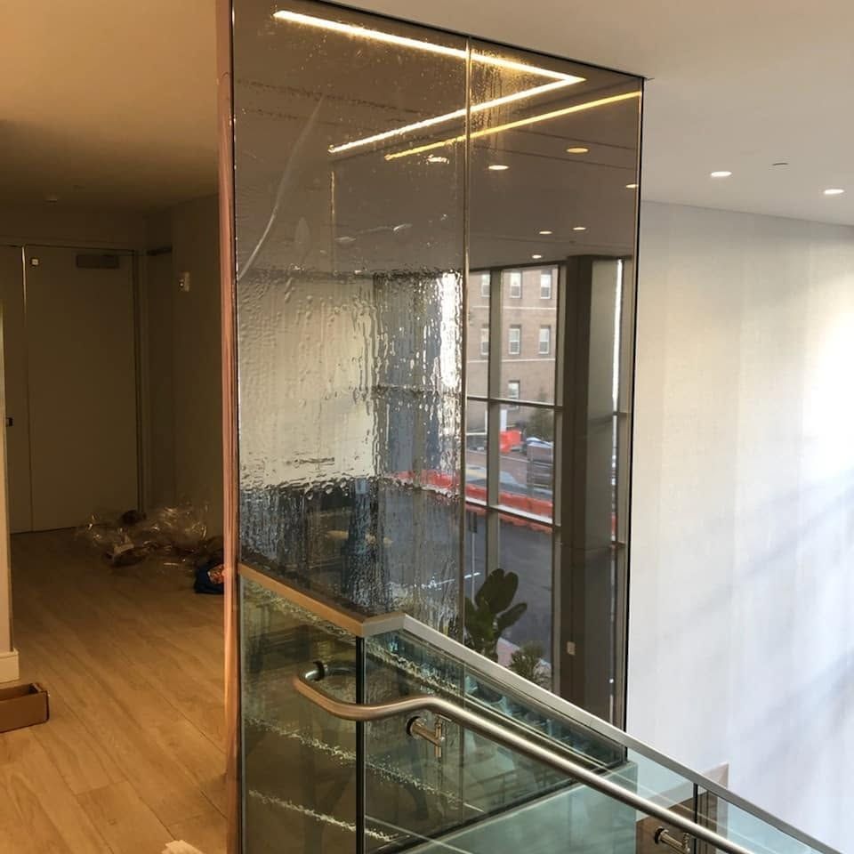 Modern indoor stairwell with glass wall, wood floor, and window view of buildings outside