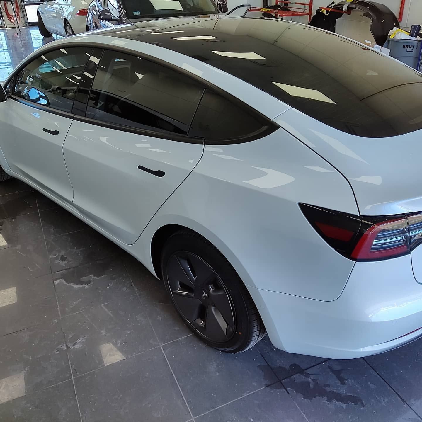 White Tesla sedan in a garage, rear side view with tinted windows and black wheels