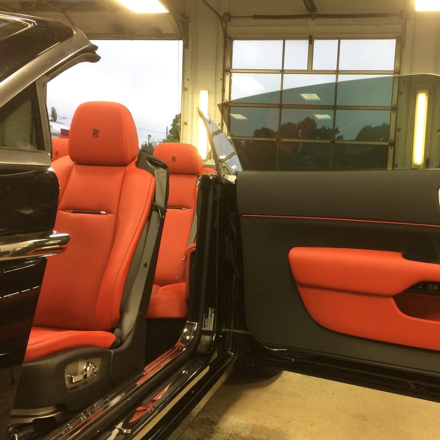Red leather car seats and open door inside a garage, showing a black-and-red luxury interior.