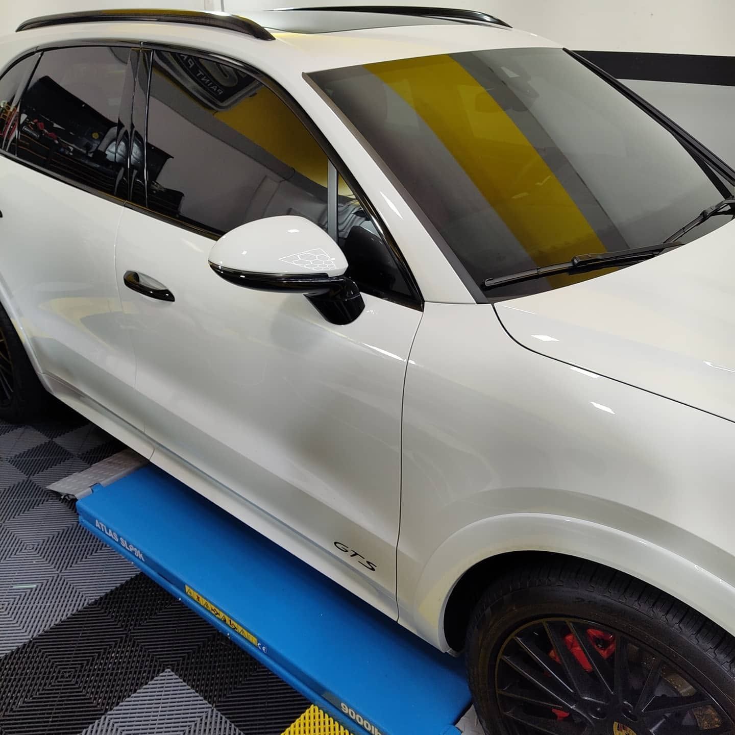 White SUV on a blue lift in a garage, shown from the side with tinted windows and black rims