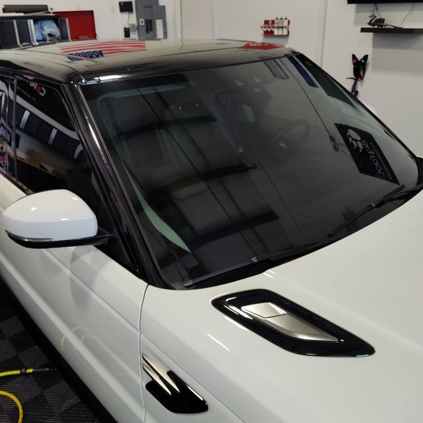 White sports car with black roof in a garage, shown from the front windshield and hood.