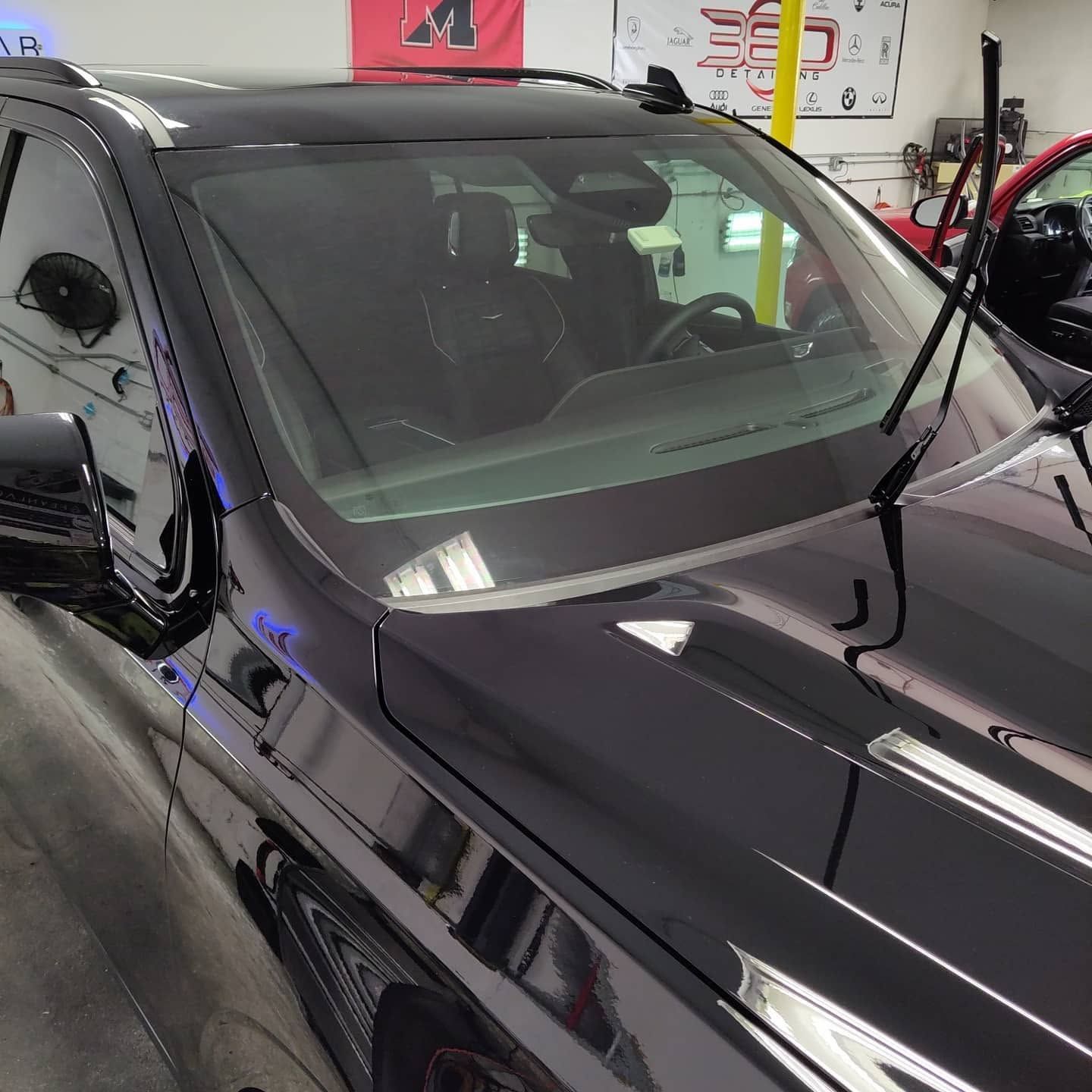 Black SUV in a garage with a windshield and hood reflecting overhead lights