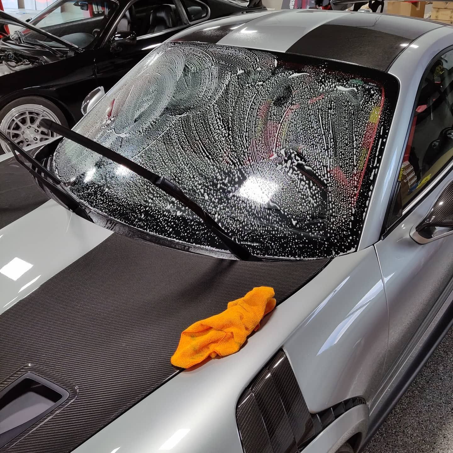 Gray sports car with shattered windshield and an orange towel on the hood in a garage