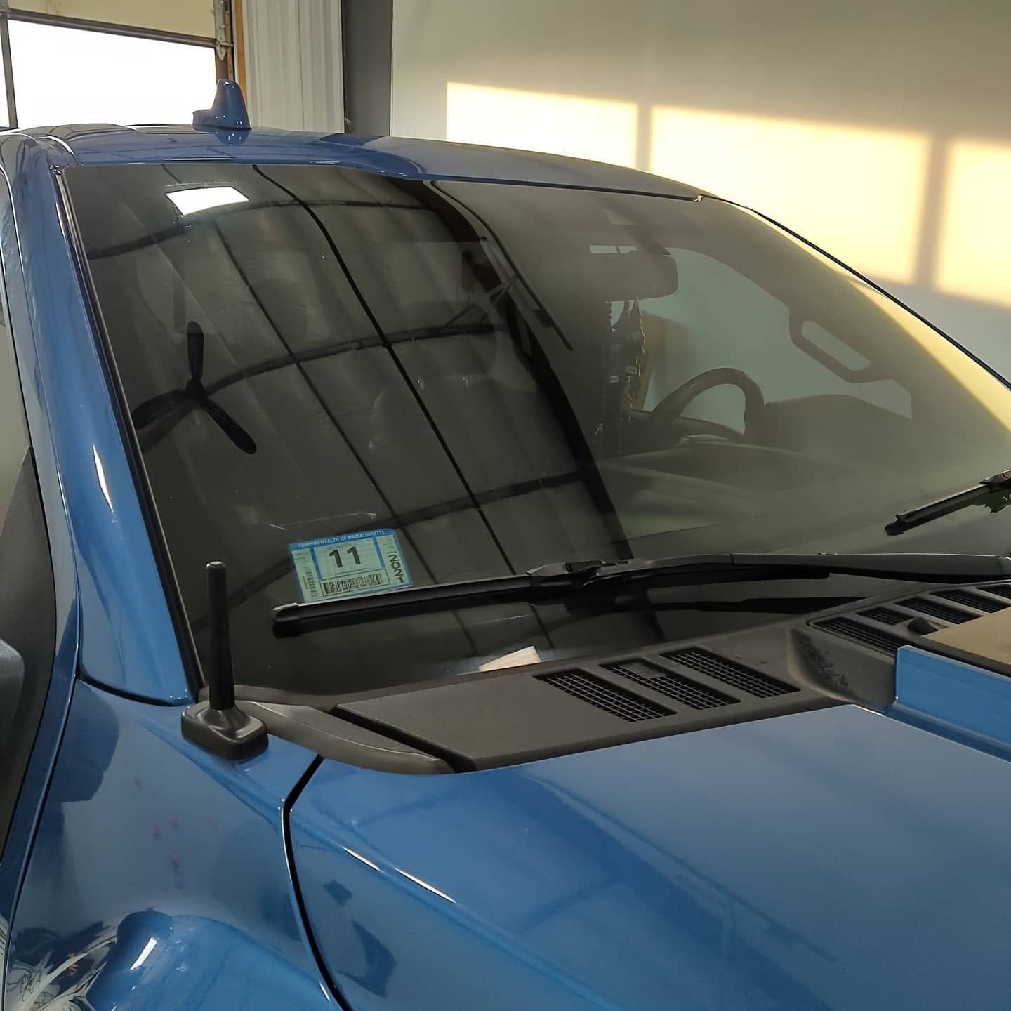 Blue car parked in a garage, showing the windshield and hood.