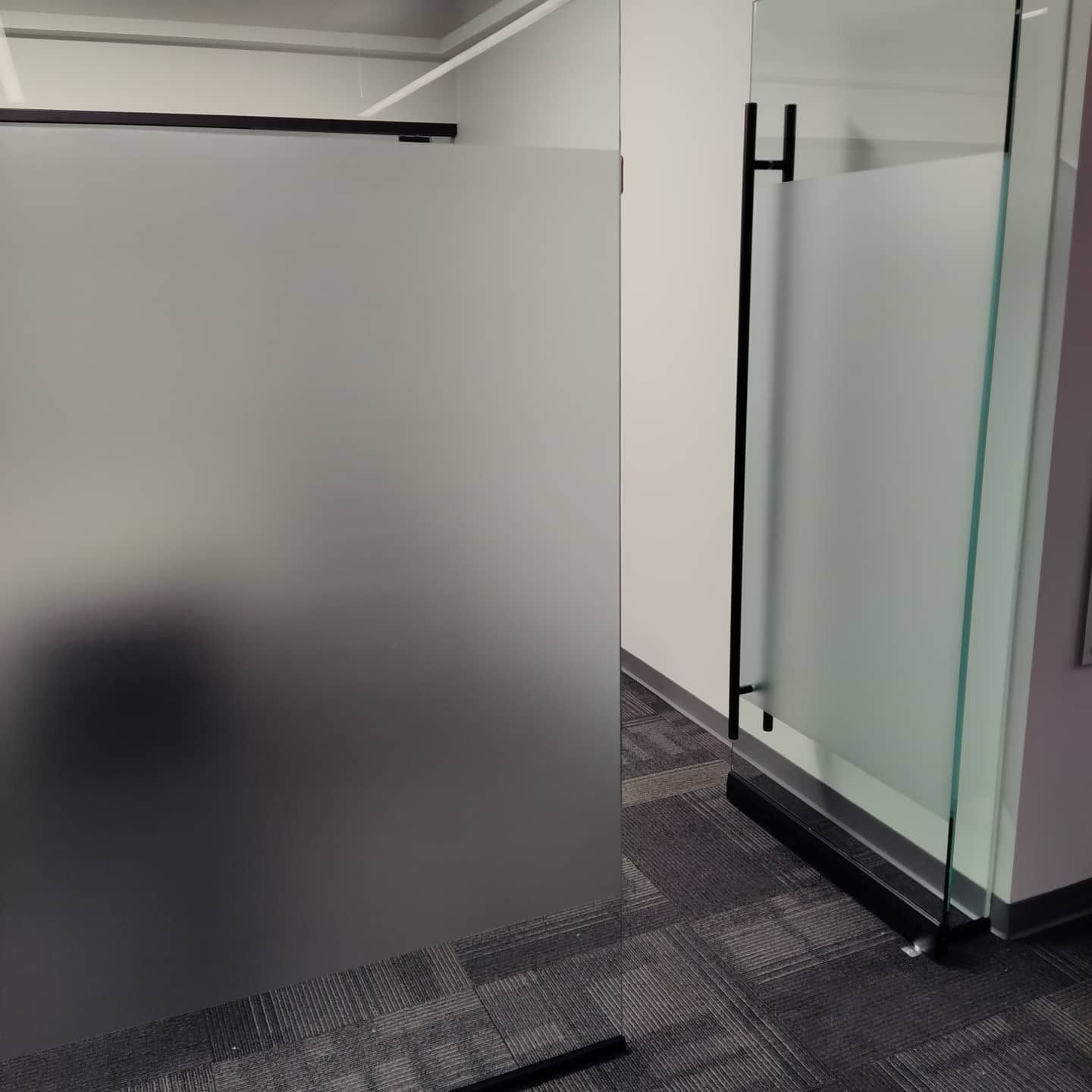 Office hallway with frosted glass partition and clear glass door panels on carpeted floor