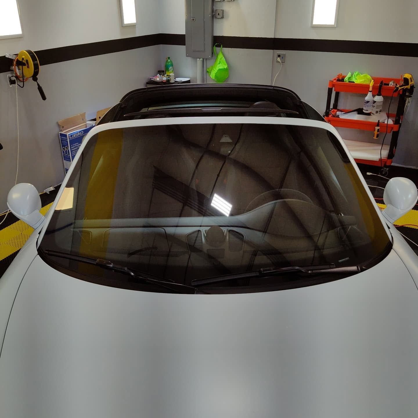 White sports car parked in a garage, viewed from the front with roof rack visible.