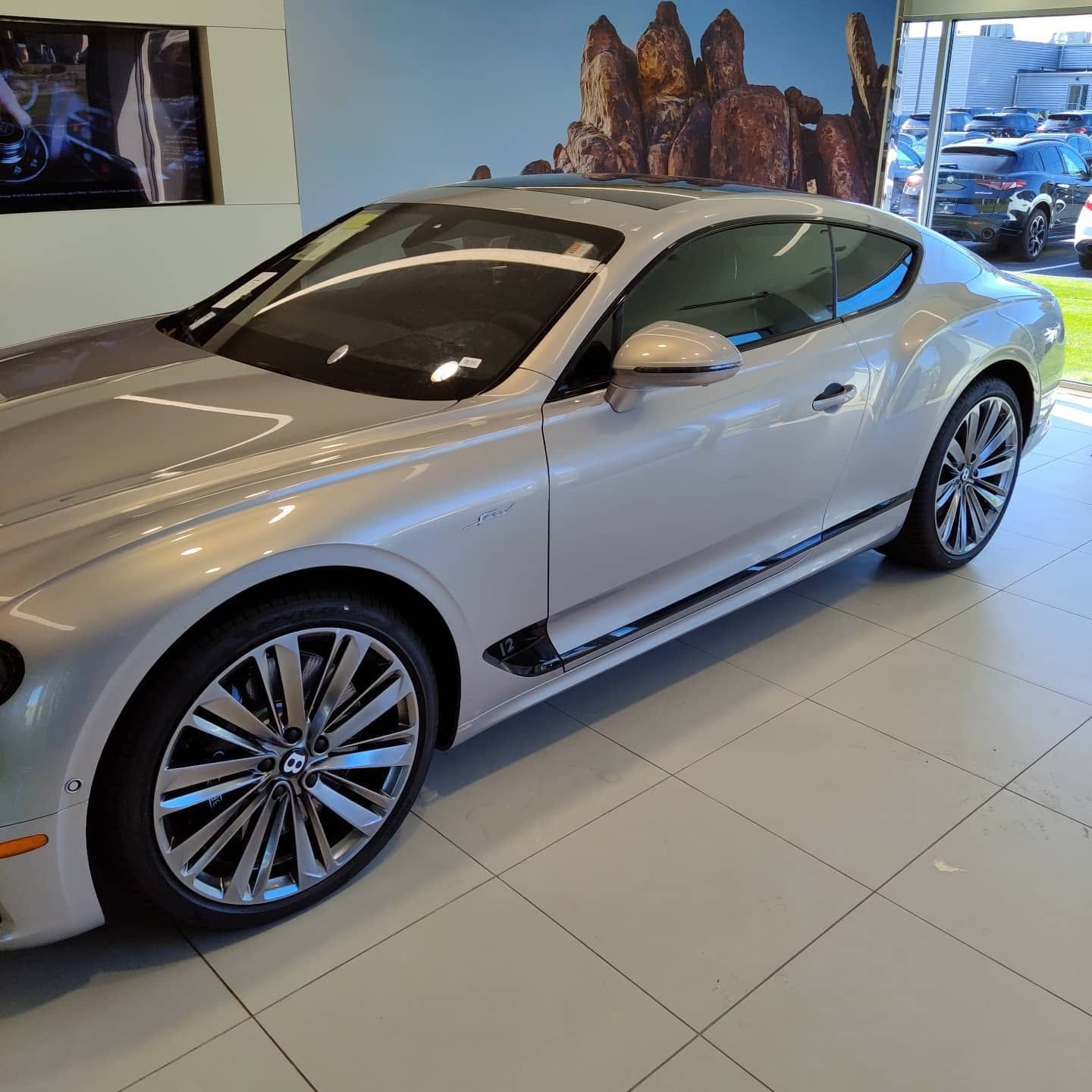 Silver luxury coupe displayed in a showroom with tiled floor and wall art
