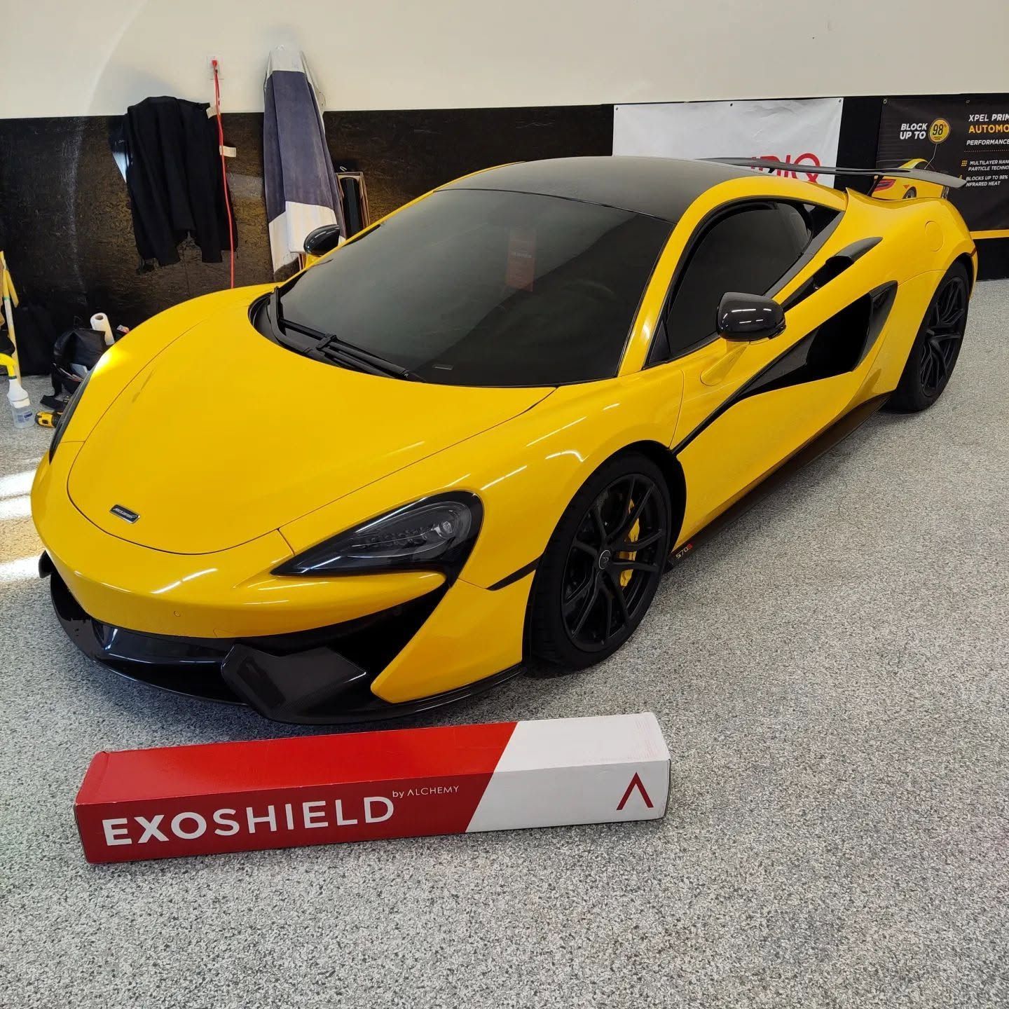 Yellow sports car on display indoors with an Exoshield sign in front