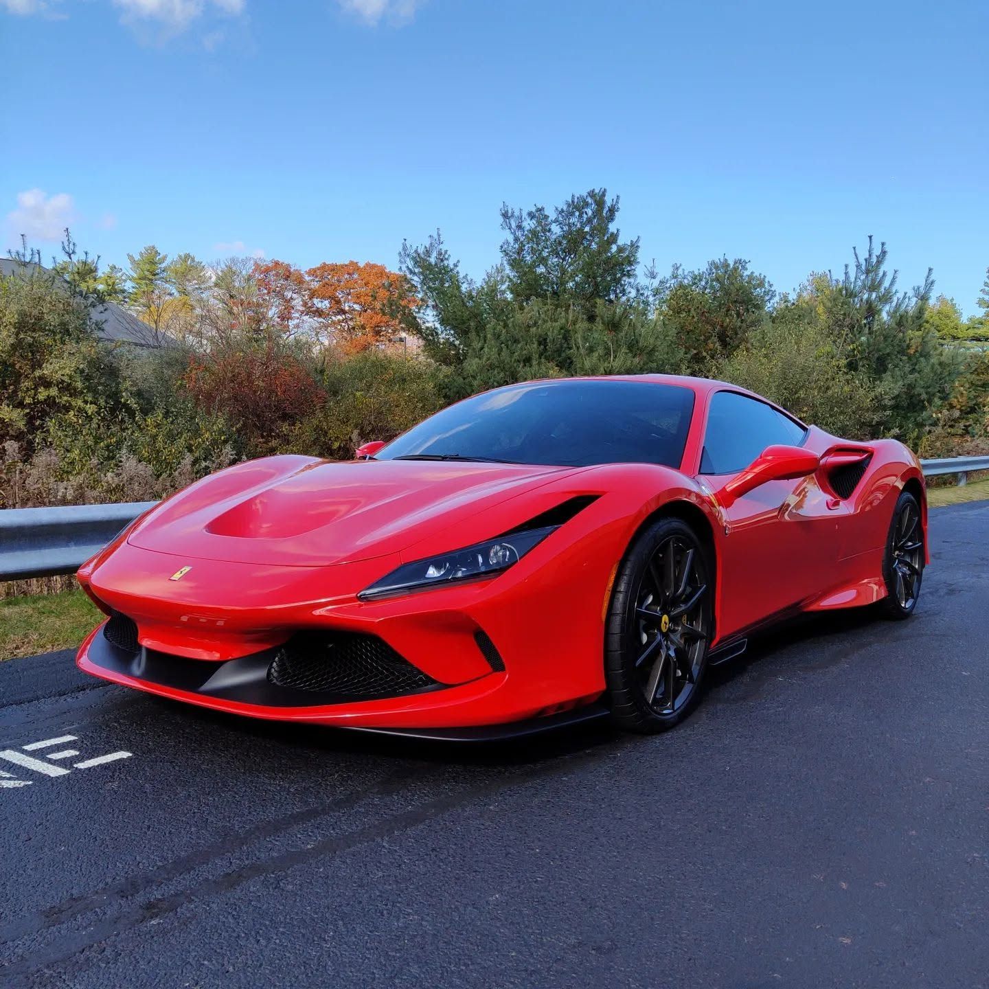Red sports car parked on a road, with trees and blue sky in the background.