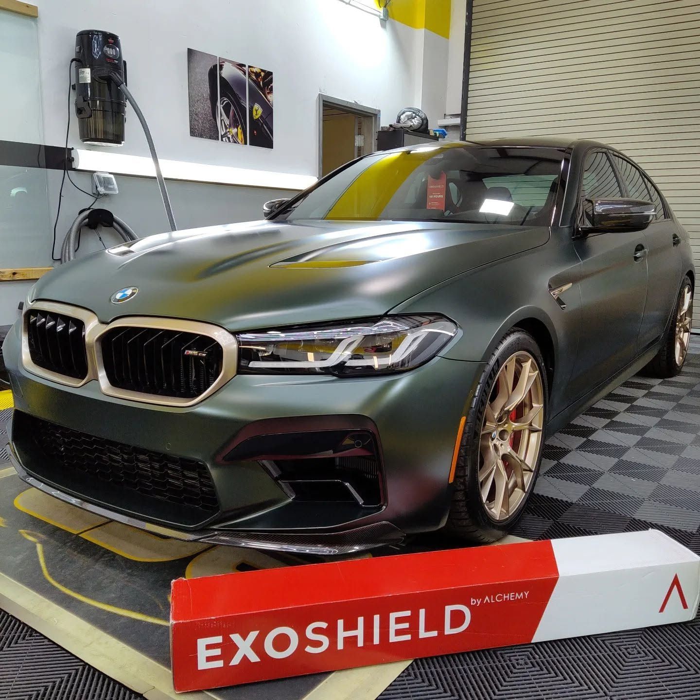 Matte green BMW sedan in a garage beside an Exoshield box