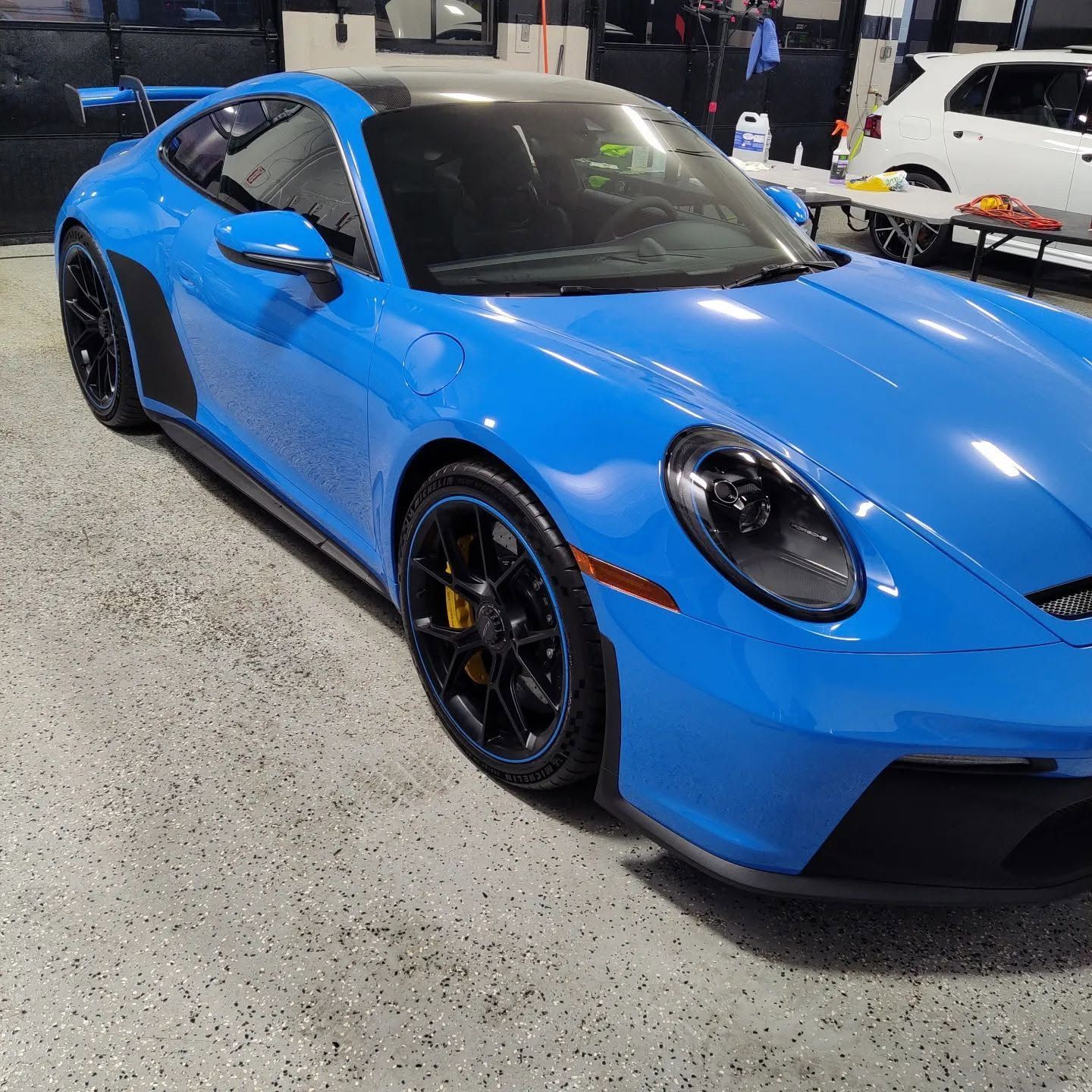 Blue sports car on display at an auto show, angled front view with black rims and dark windows