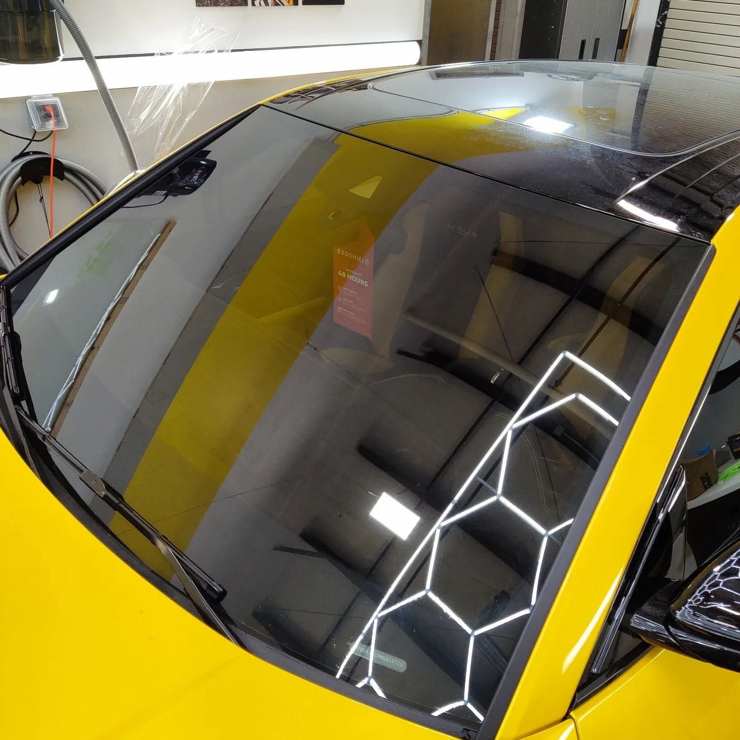 Yellow sports car with a glossy black windshield reflecting ceiling lights in a workshop