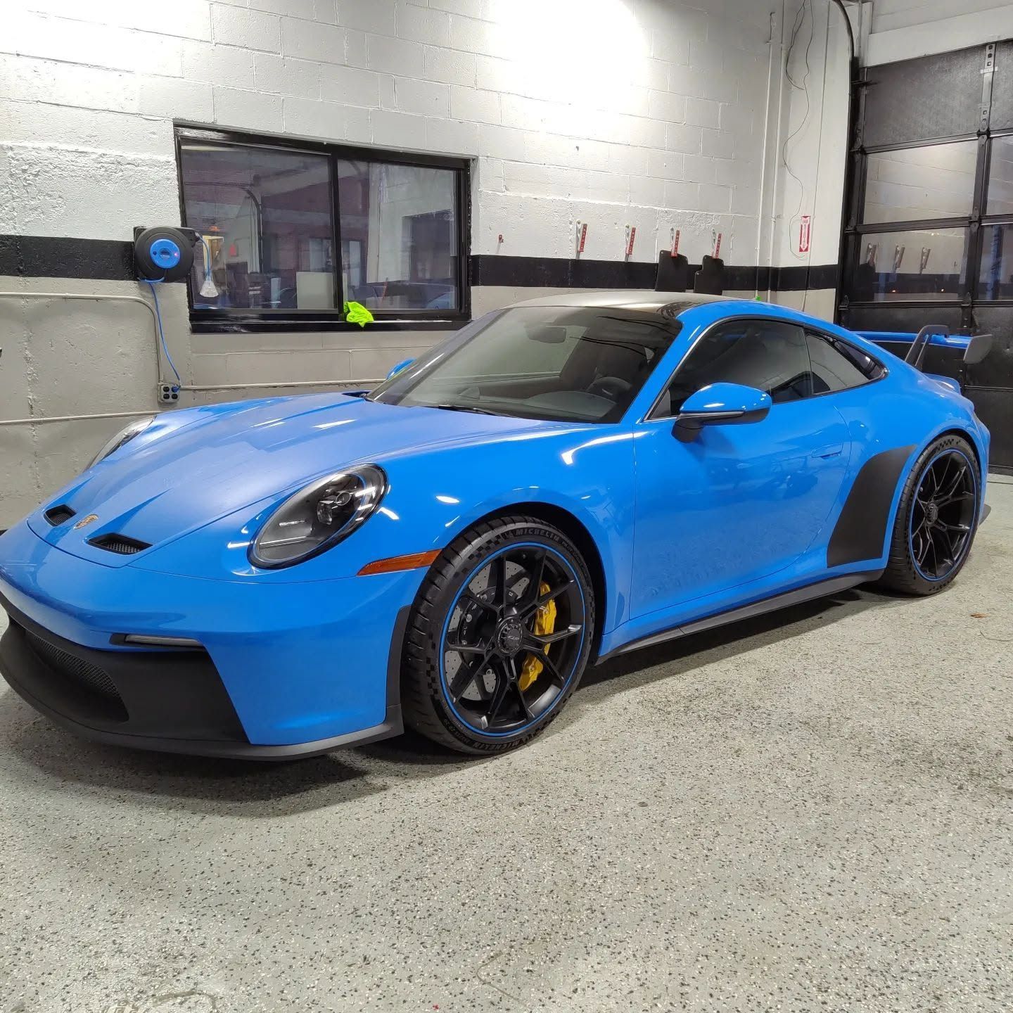 Blue sports coupe parked indoors in a garage, viewed from the front-left side.