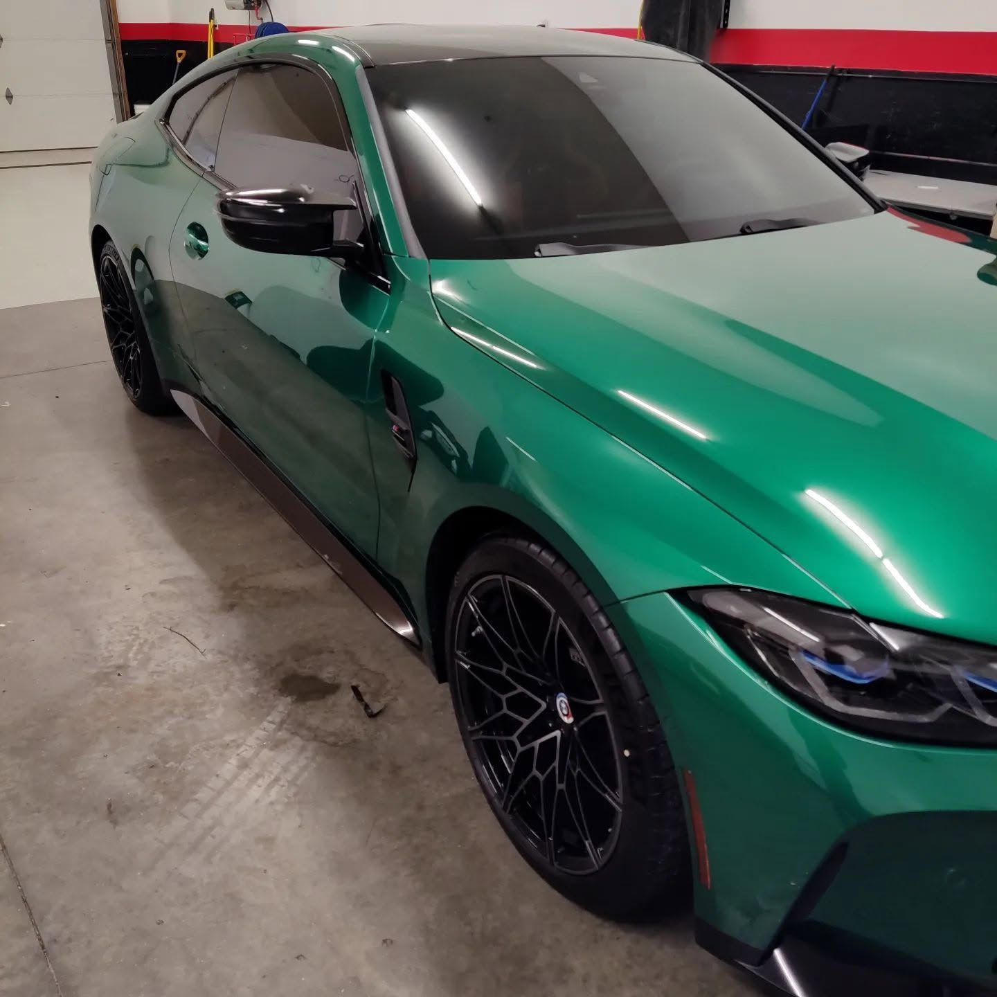 Green BMW sedan parked indoors in a garage, shown from the front side angle.