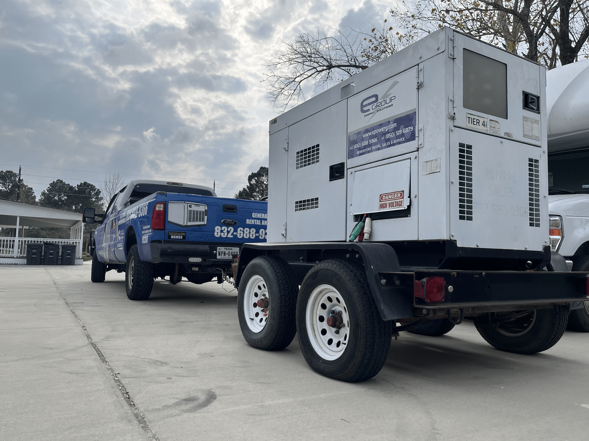 Blue pickup towing white industrial generator on a paved lot under cloudy sky