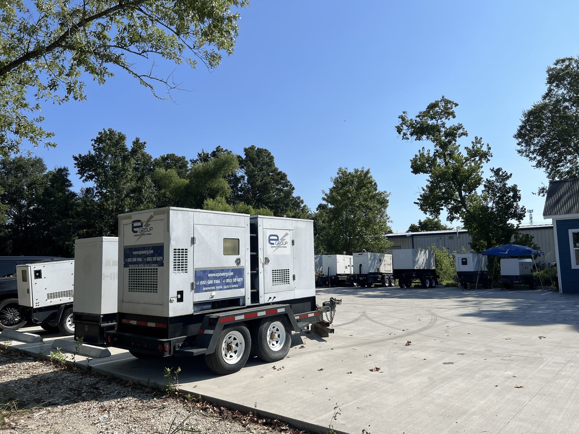 White utility trailers parked in a gravel lot with trees and trucks in the background