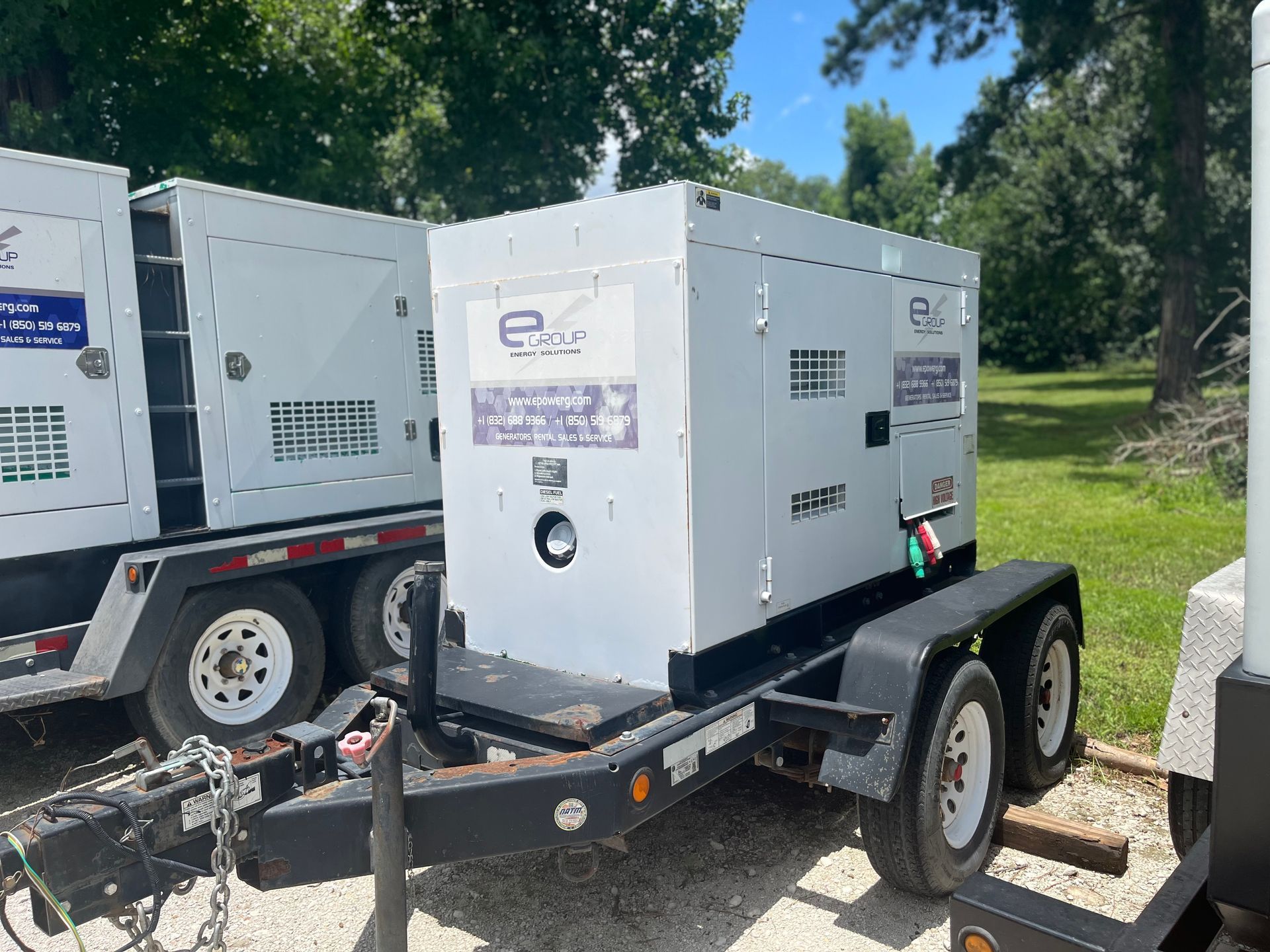 White towable generator trailer parked outdoors beside another generator on a sunny grassy lot
