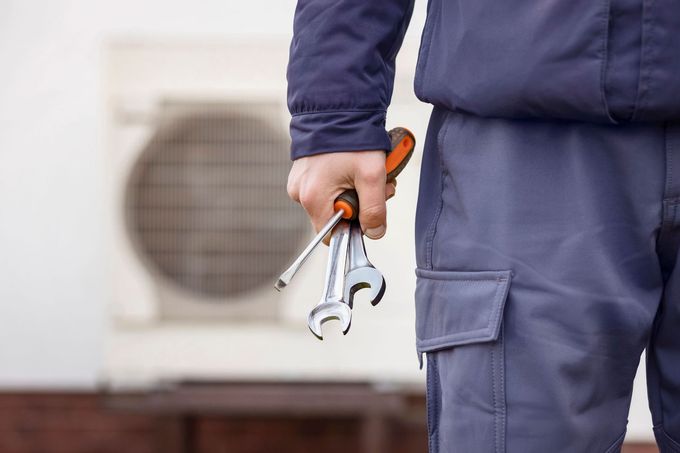 Technician in navy uniform holding a wrench beside an outdoor HVAC unit