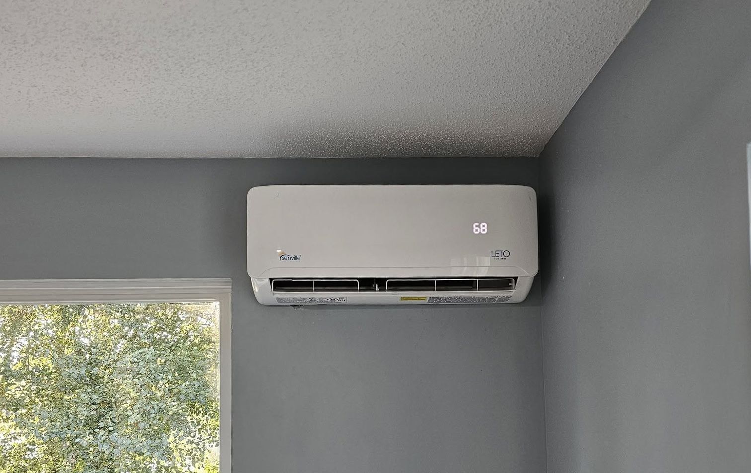Wall-mounted white air conditioner on a gray wall near a window
