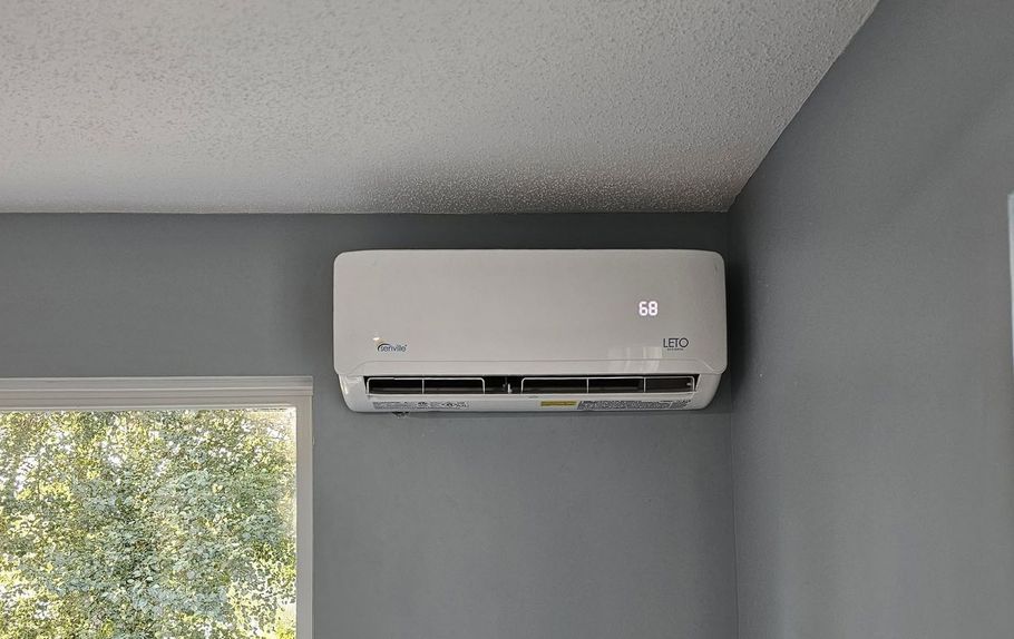 Wall-mounted white air conditioner on a gray wall near a window
