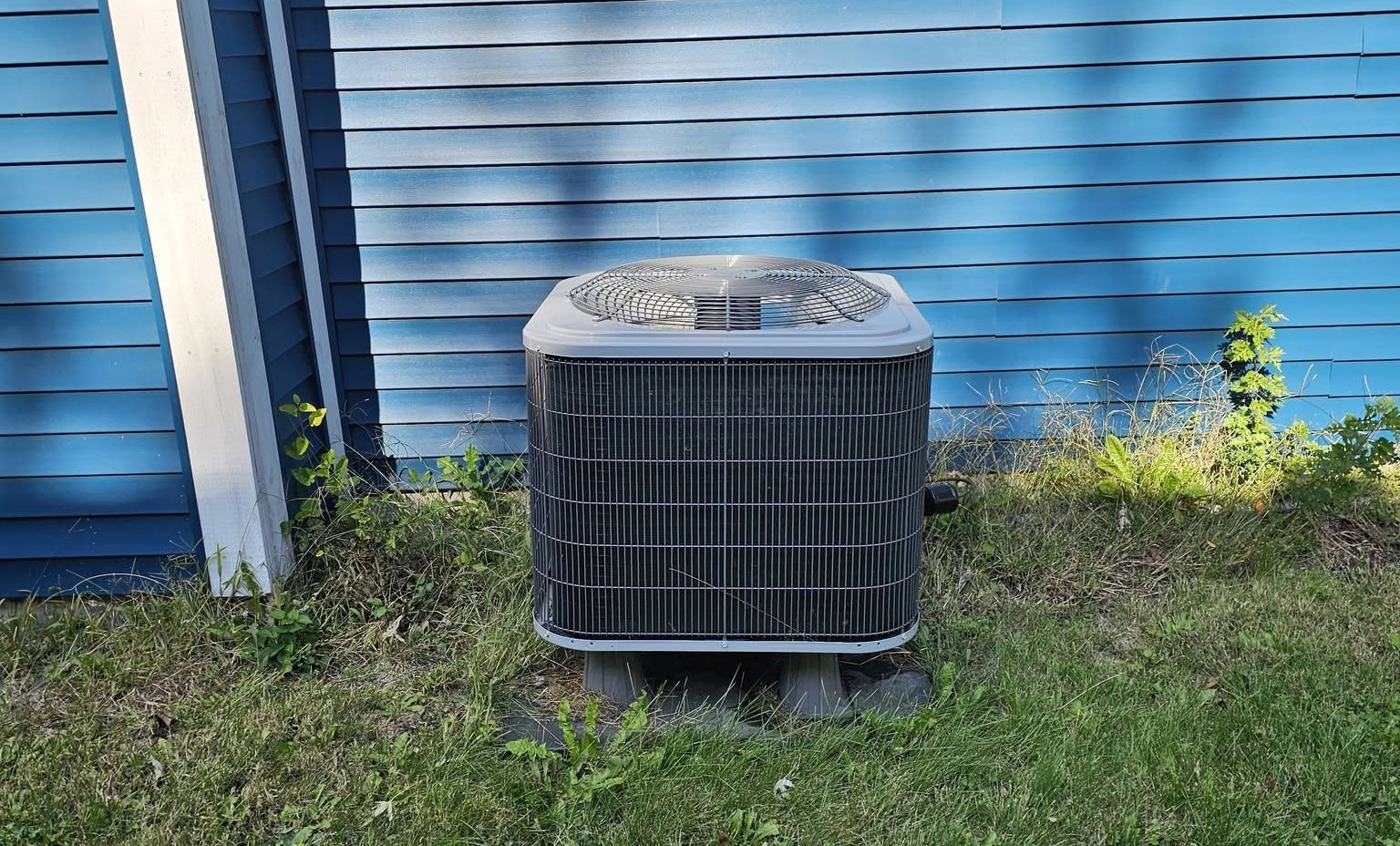 Outdoor air conditioning unit beside a blue house wall on grass