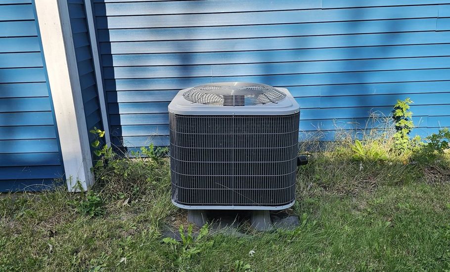 Outdoor air conditioning unit beside a blue house wall on grass