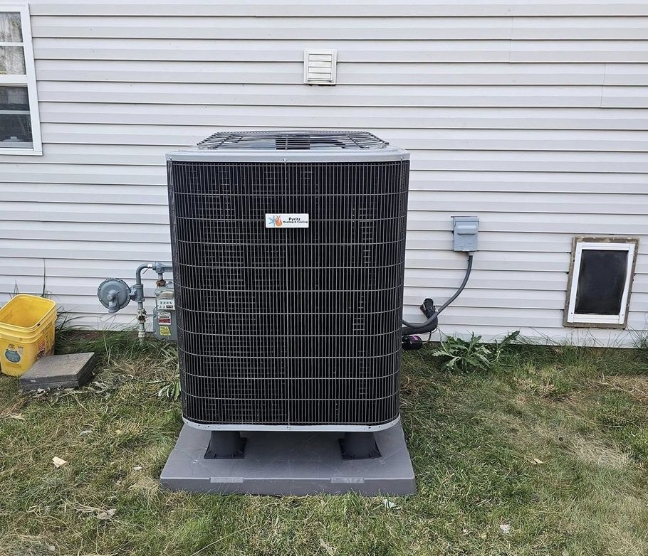 Outdoor HVAC condenser unit with black protective cover beside a house wall on a concrete pad.