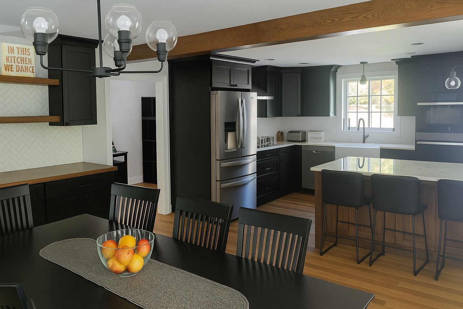 Modern kitchen with black cabinets, stainless steel refrigerator, and a dining table with fruit.