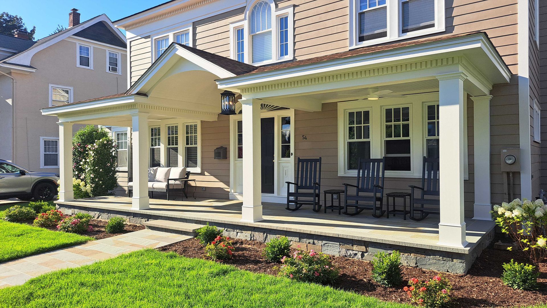 A house with a porch, rocking chairs, and flower beds in front.