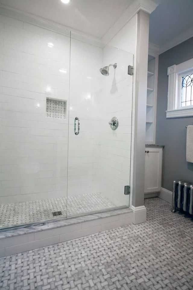 Bathroom with white tiled shower, glass door, gray tiled floor, built-in shelves, and radiator.