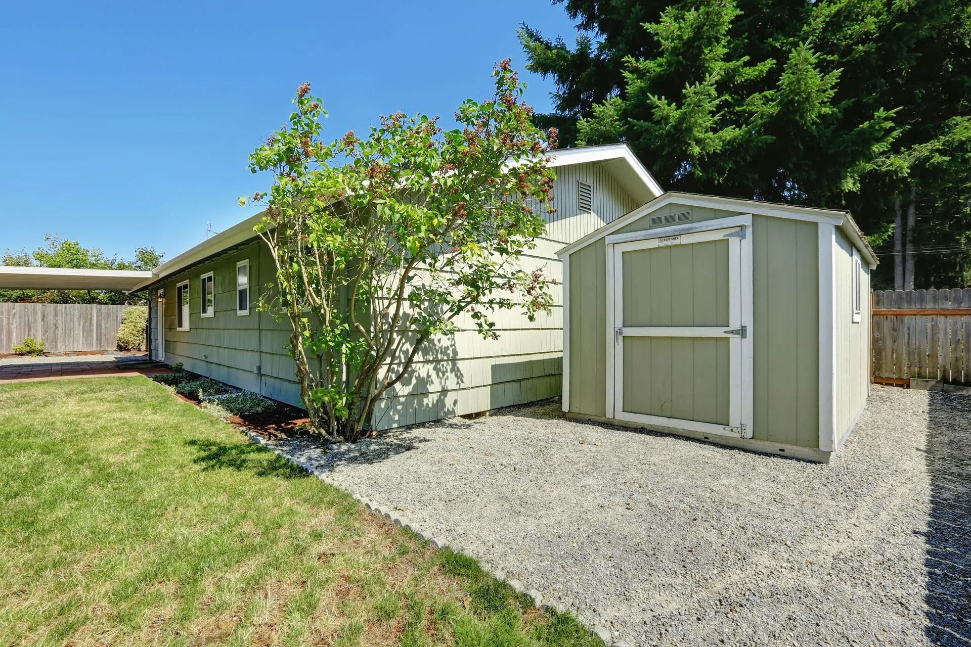 Green house and shed next to gravel path and grass lawn. Bright sunny day.